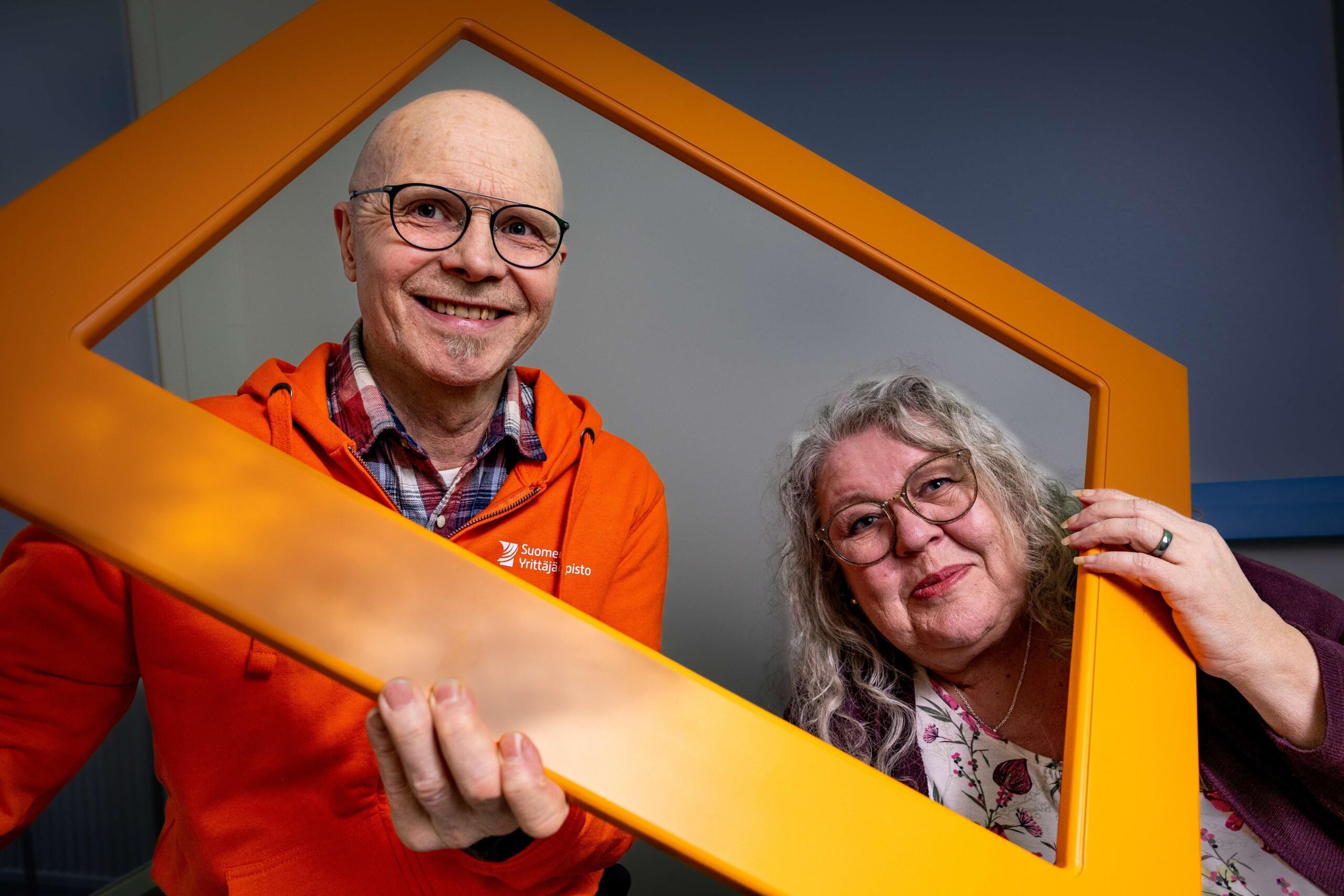 Kaksi Suomen Yrittäjäopiston kouluttajaa kurkkaavat kehyksen läpi iloisesti.